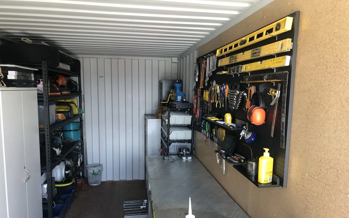 Inside Ned Coten's own shipping container: a tool wall with spirit levels and spanners, a steel workbench, and shelves of power tools