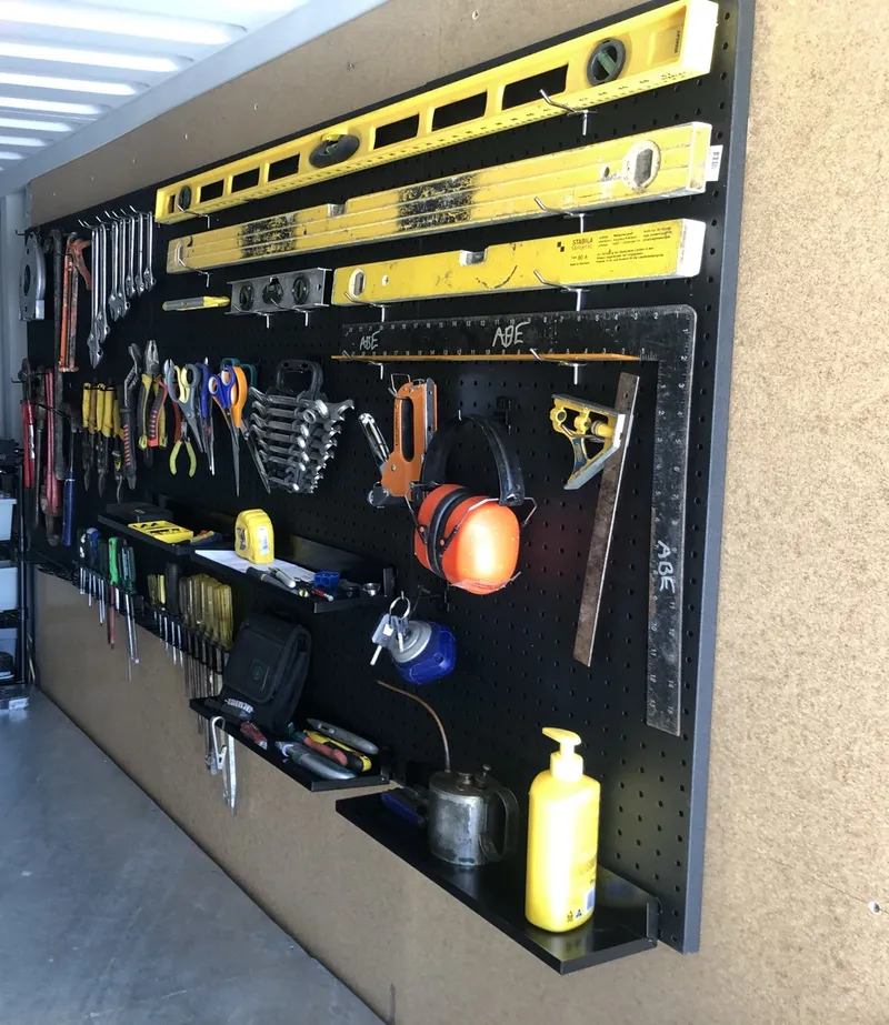 Pegboard tool wall in Ned's container, with yellow spirit levels, spanners, screwdrivers, pliers and ear muffs above a steel workbench